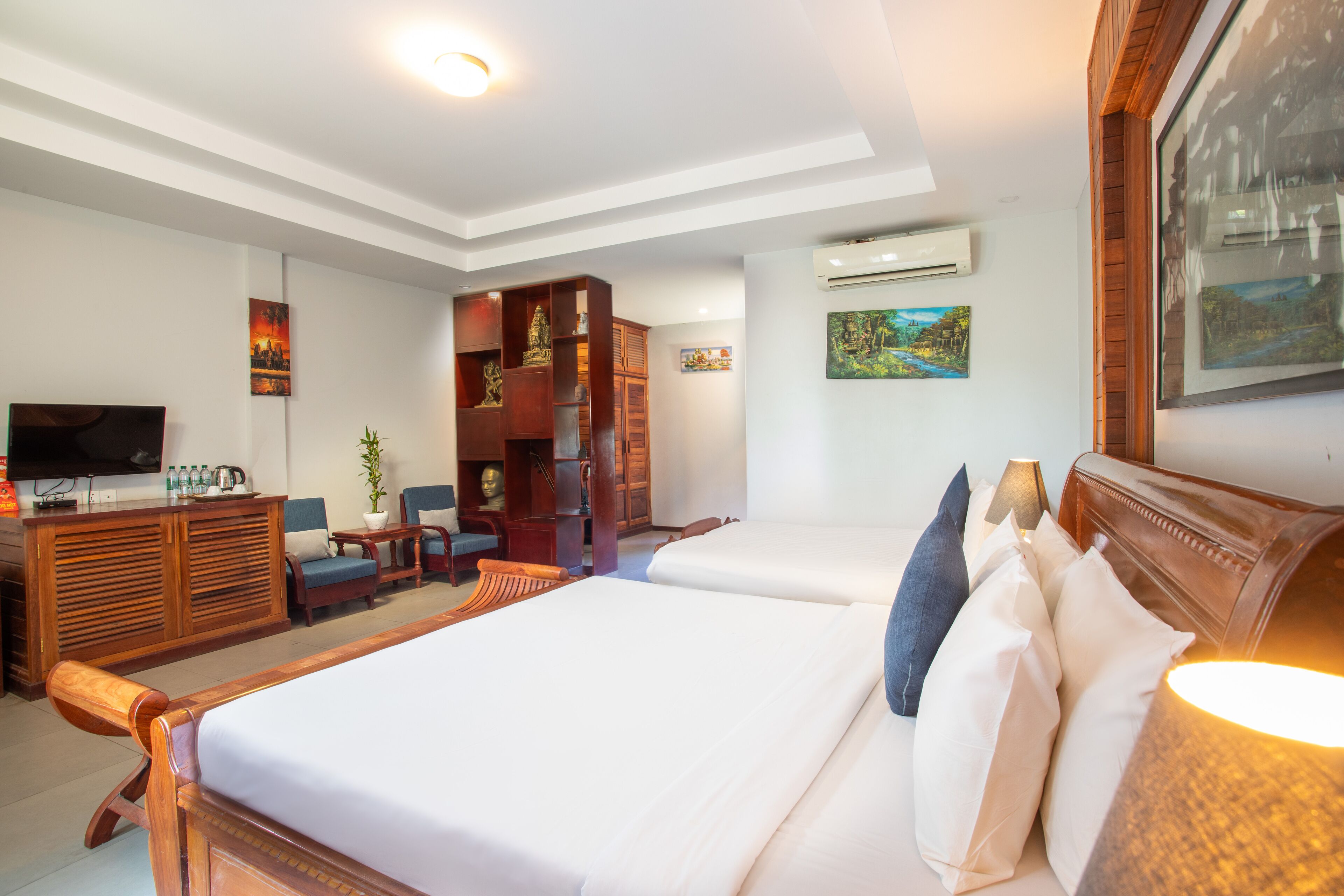 Habitación de hotel con dos camas, un televisor, un armario de madera y una estantería.