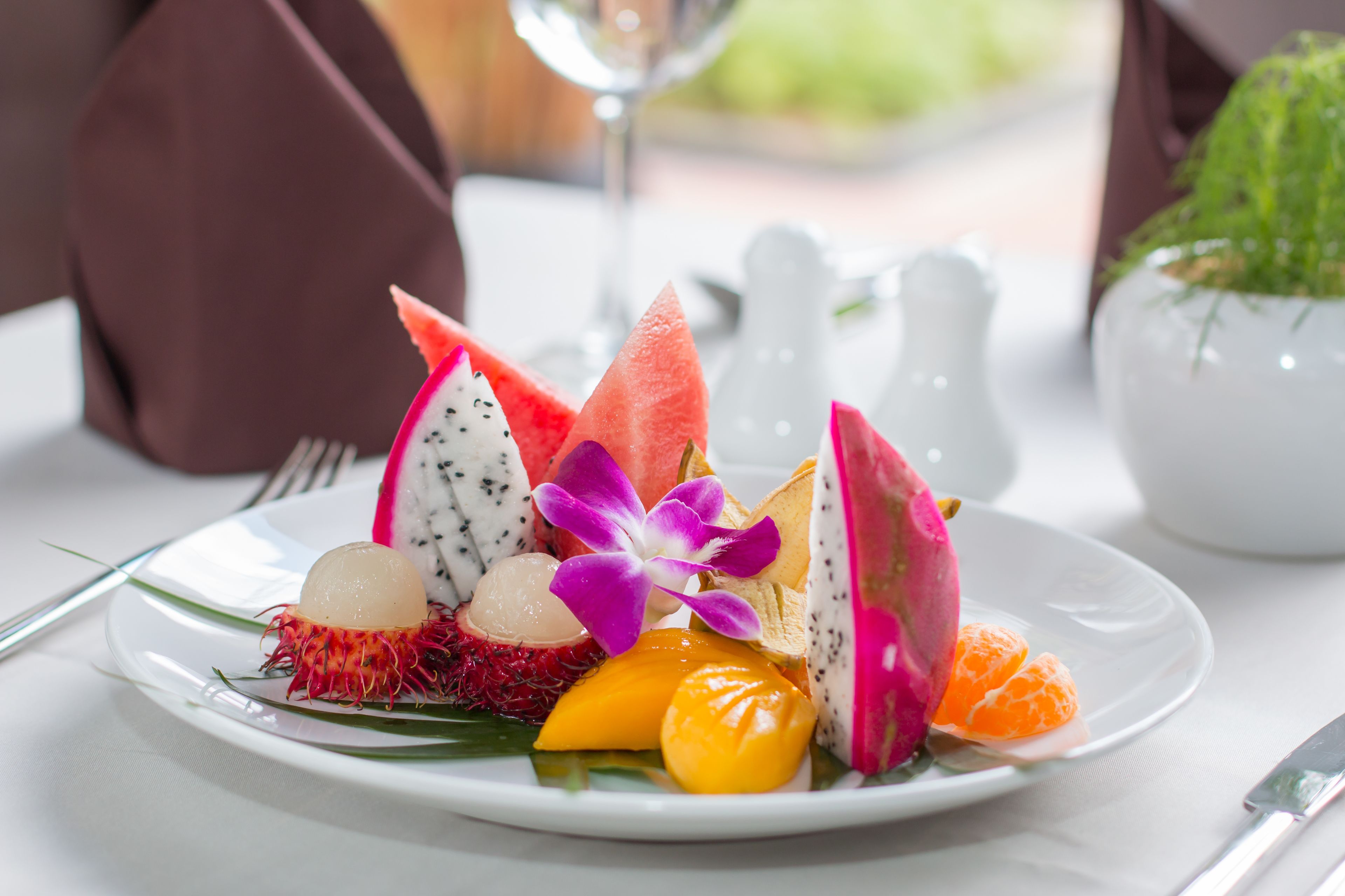 A plate of assorted fruits and a purple flower on a white plate.