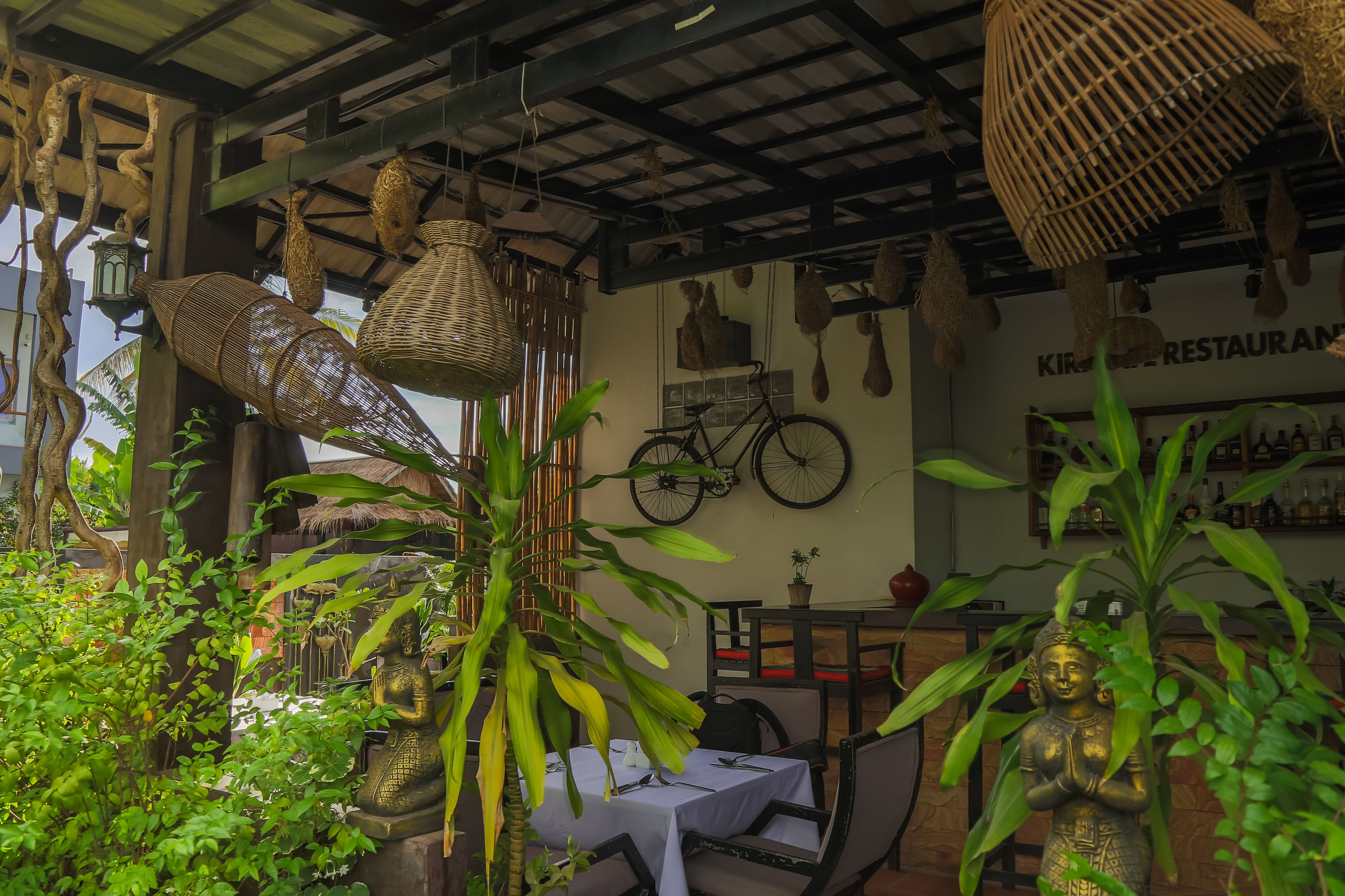 A restaurant with wicker hanging lamps, a bicycle, and a statue of a deity.