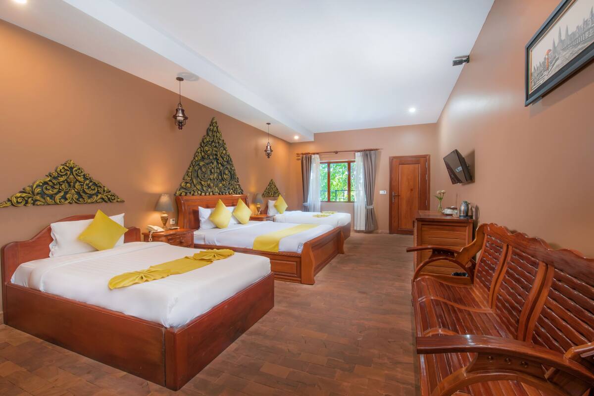 A hotel room with two beds, a wooden bench, a desk, and a large window.