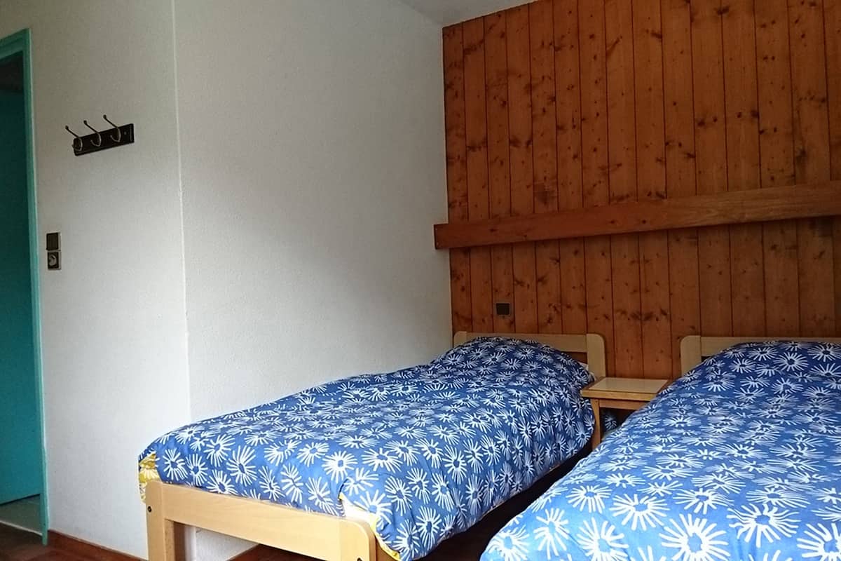 A room with two single beds, wooden walls, a blue door, and a small table.