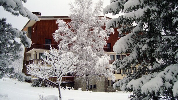 Ein schneebedecktes Gebäude mit einer Holzfassade und mehreren Balkonen.