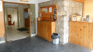 Ein Empfangsbereich mit einer Steinwand, Holzschränken, einem Mülleimer und einem Schwarzebrett mit Aushängen.