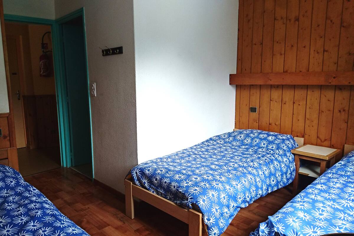 A room with two single beds with matching blue floral bedding, wooden headboards, and a wooden wall panel.