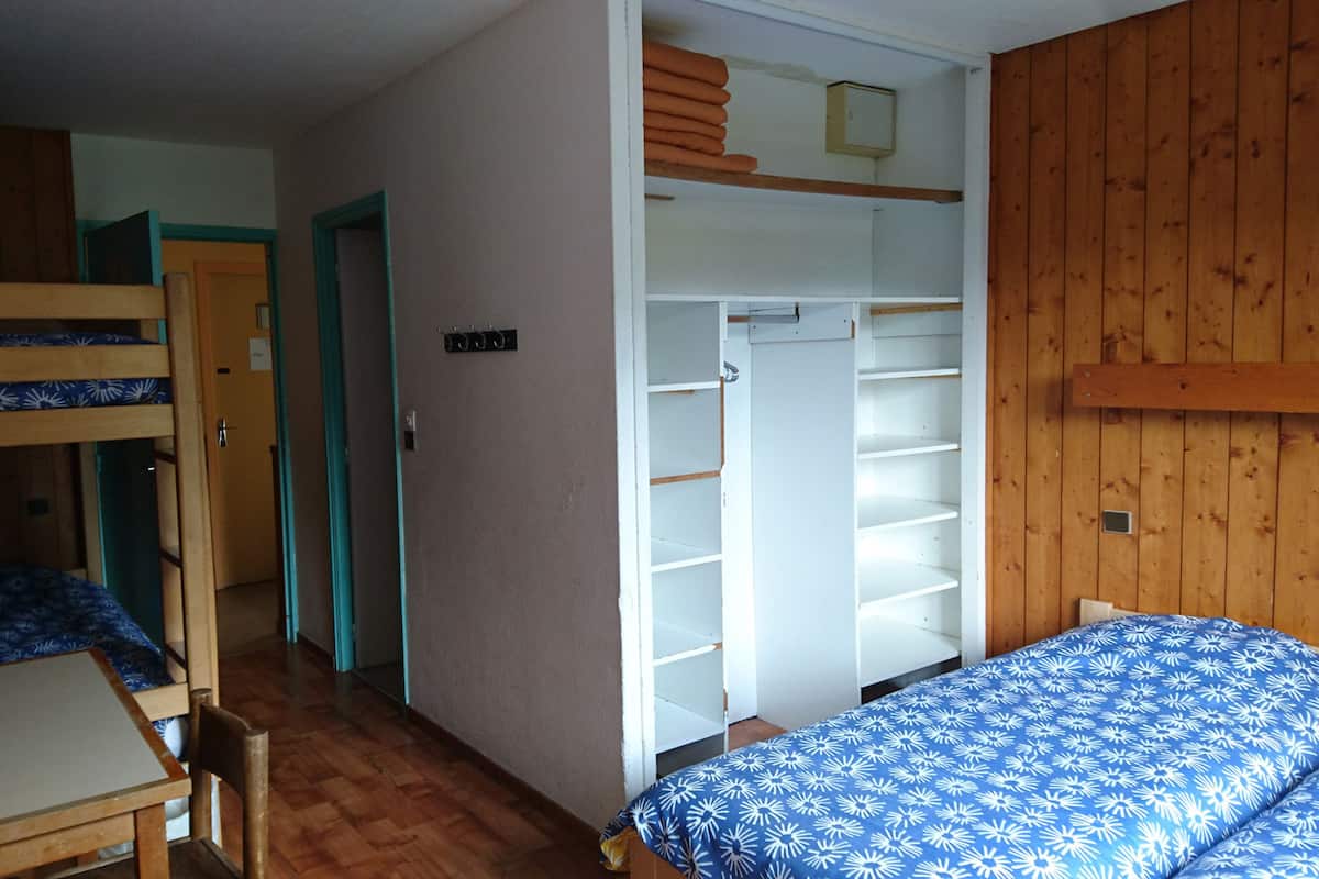 A room with bunk beds, a desk, a wardrobe, and a bed with a patterned bedspread.