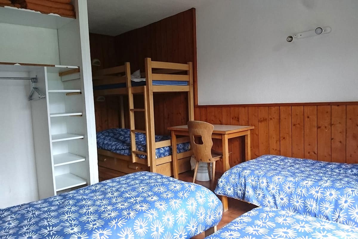 A dormitory room with bunk beds, a desk, and a chair.