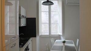 A kitchen with white cabinets, a black stove, a window with white frames, and a table with chairs. - B&B Girovagando (Rome)