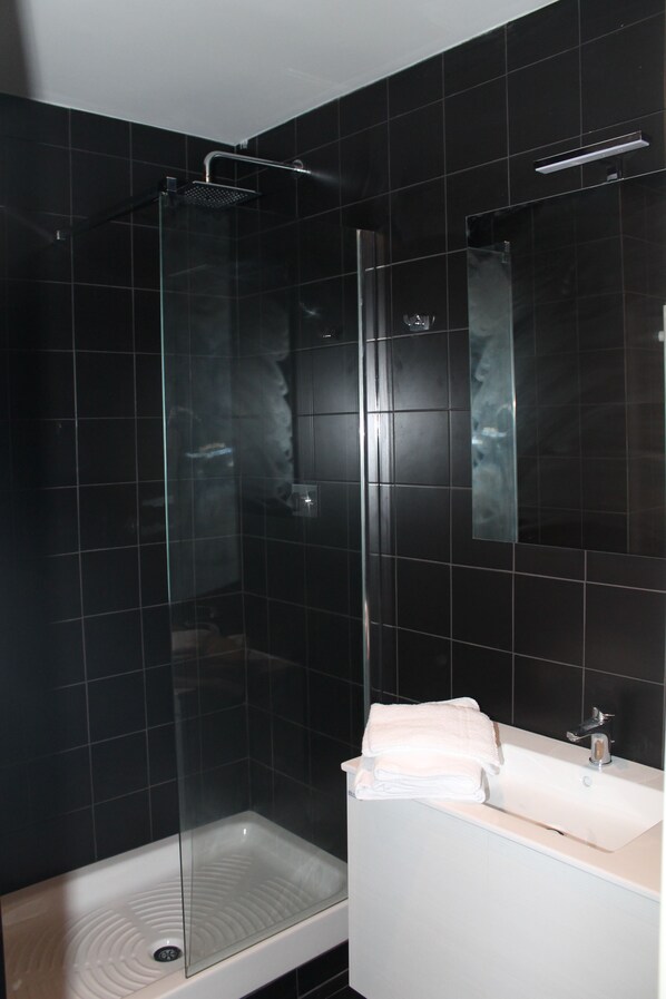Un baño moderno con ducha de vidrio, lavamanos blanco y un espejo grande.