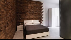 A modern bedroom with a wooden accent wall, a white bed, and a wardrobe. - B&B Girovagando (Rome)