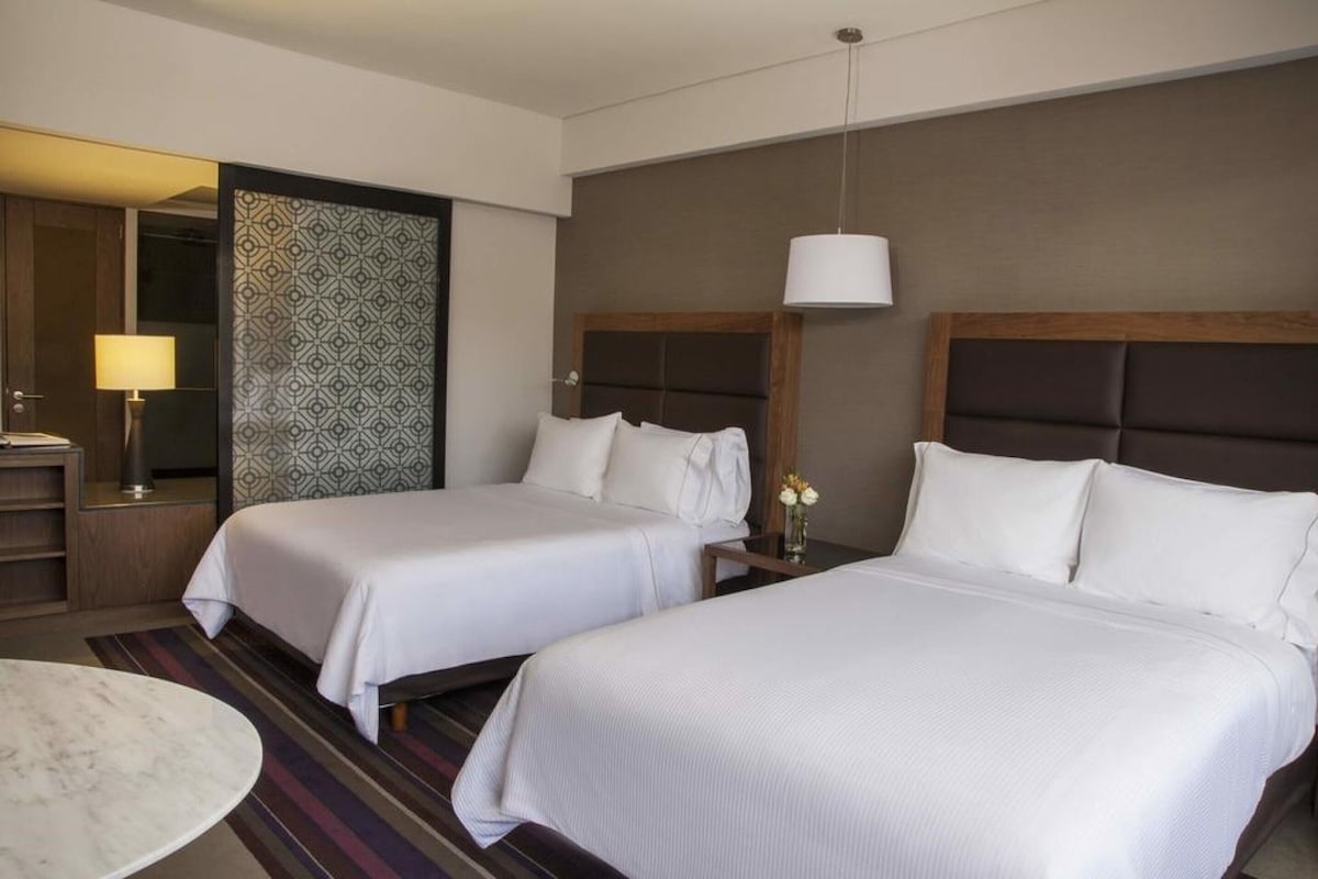 Une chambre d’hôtel avec deux lits, une table de chevet avec une lampe, un miroir et un mur décoré d’un motif.