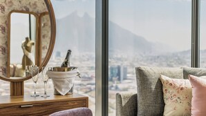 Een kamer met een houten dressoir, een spiegel, twee champagnefluiten en een emmer met een fles. Een fauteuil met bloemenkussens is zichtbaar.