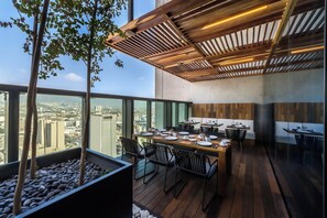 Un espace repas moderne avec une longue table dressée pour quatre personnes, entourée de chaises noires, et une vue sur la ville grâce à de grandes fenêtres.