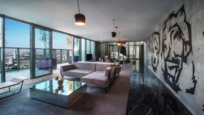 Een moderne woonkamer met een grote hoekbank, een glazen salontafel en een uitzicht op de stad door middel van ramen van de vloer tot aan het plafond.