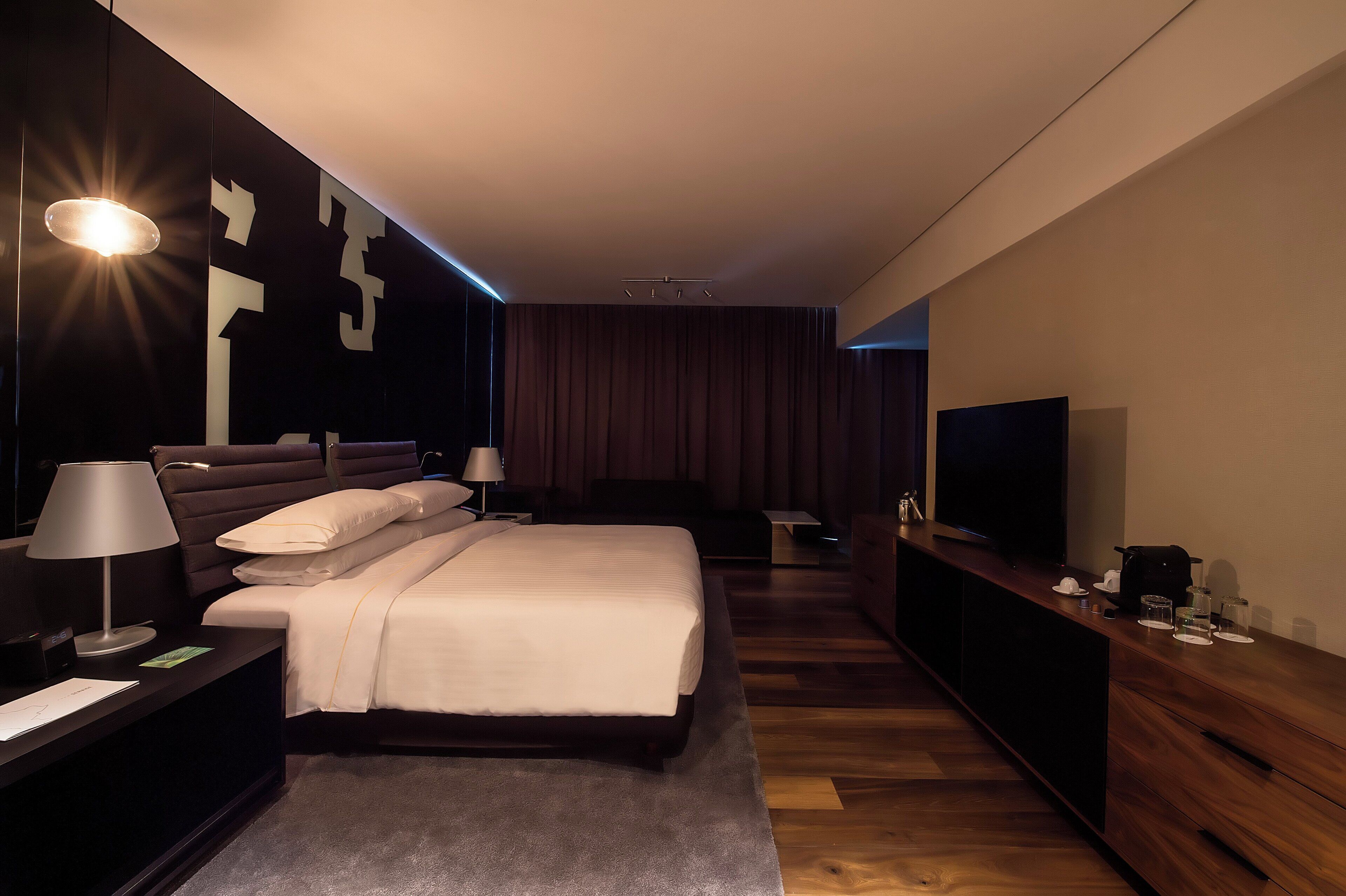Una habitación de hotel moderna con una cama grande, mesitas de noche, un televisor y una consola de madera.