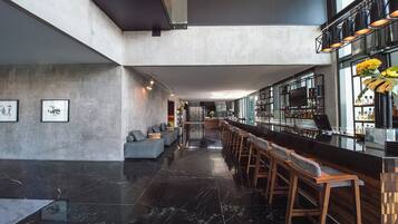 Zona de bar moderna con techo alto, suelo de mármol y una barra larga con taburetes.