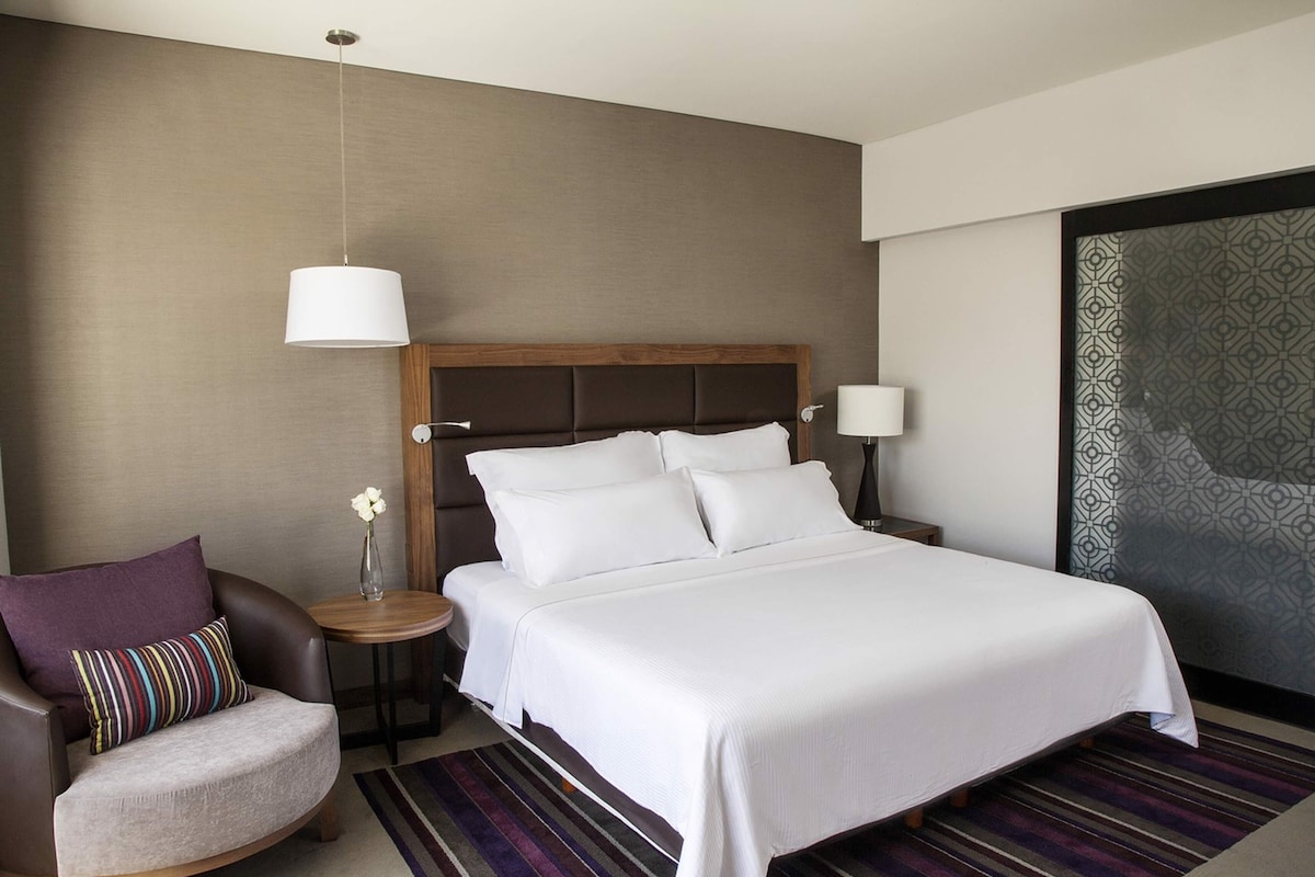 Une chambre d’hôtel avec un grand lit, une chaise, une table de chevet et une lampe.