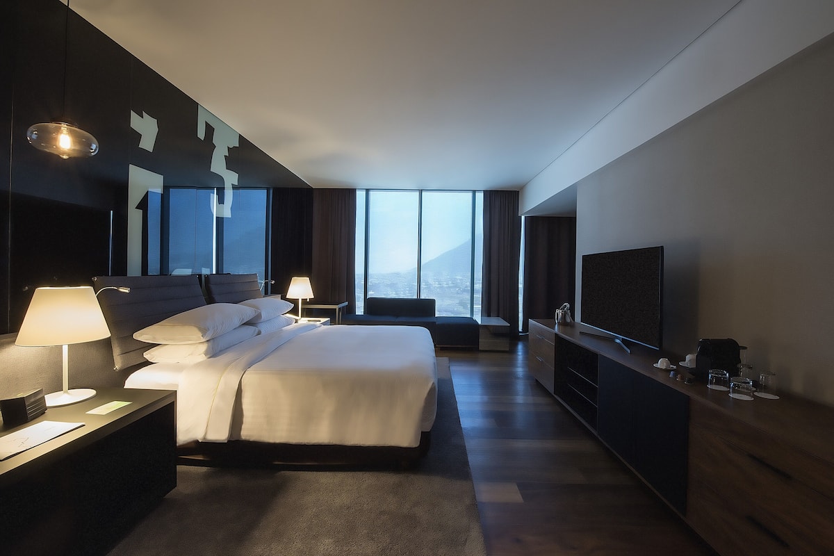 Une chambre d’hôtel moderne avec un grand lit, des lampes de chevet, une télévision et une vue sur la montagne.