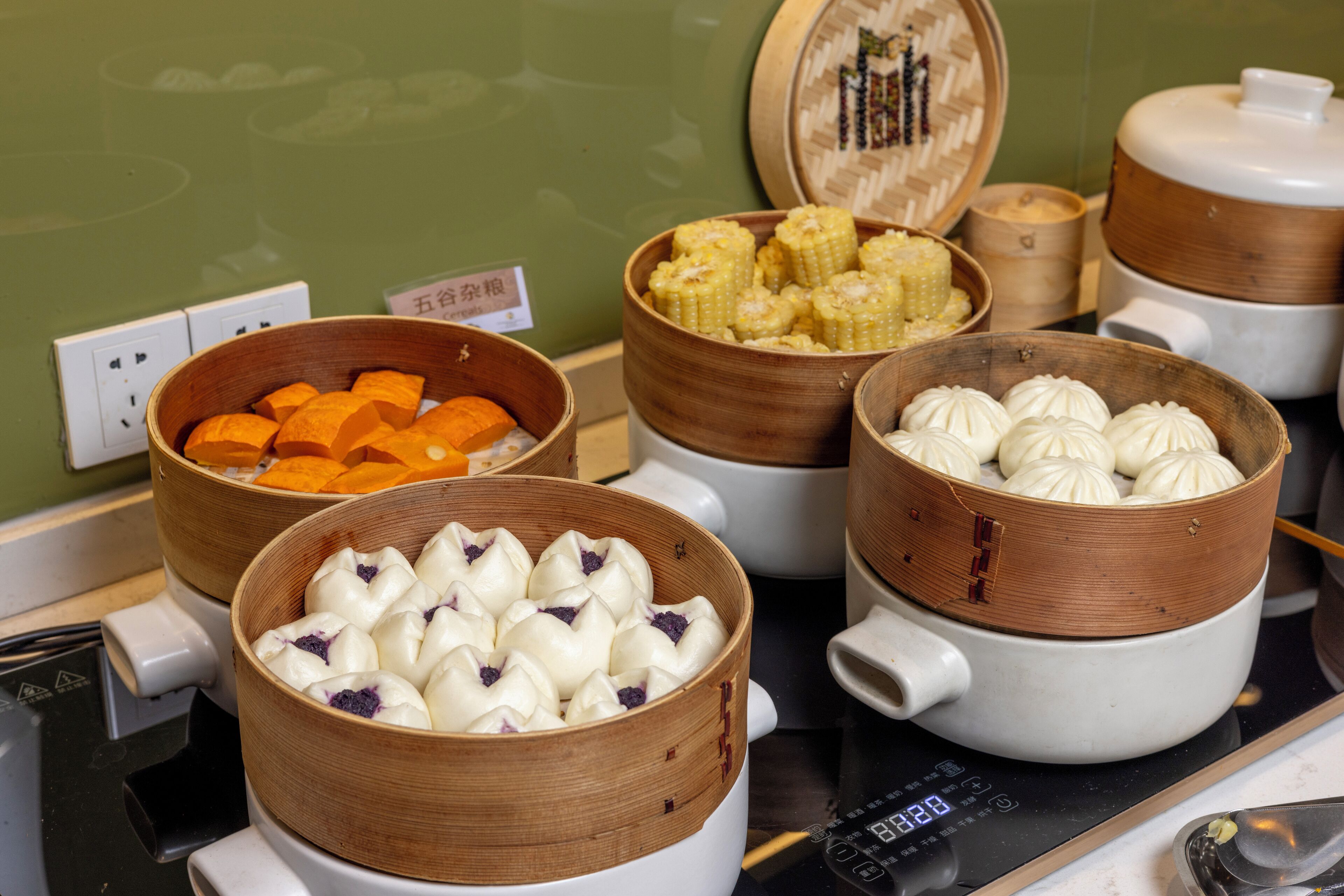 A kitchen with multiple bamboo steamers containing various types of dumplings and corn on the cob.