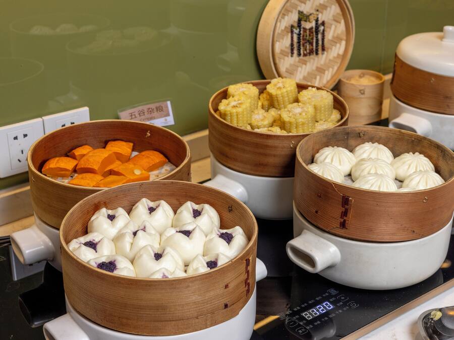 A kitchen with multiple bamboo steamers containing various types of dumplings and corn on the cob.