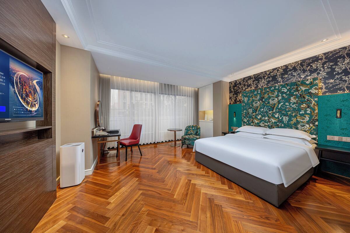 Ein modernes Hotelzimmer mit einem großen Bett, einem Schreibtisch mit Stuhl, einem Fernseher und einer Dekoration an der Wand.