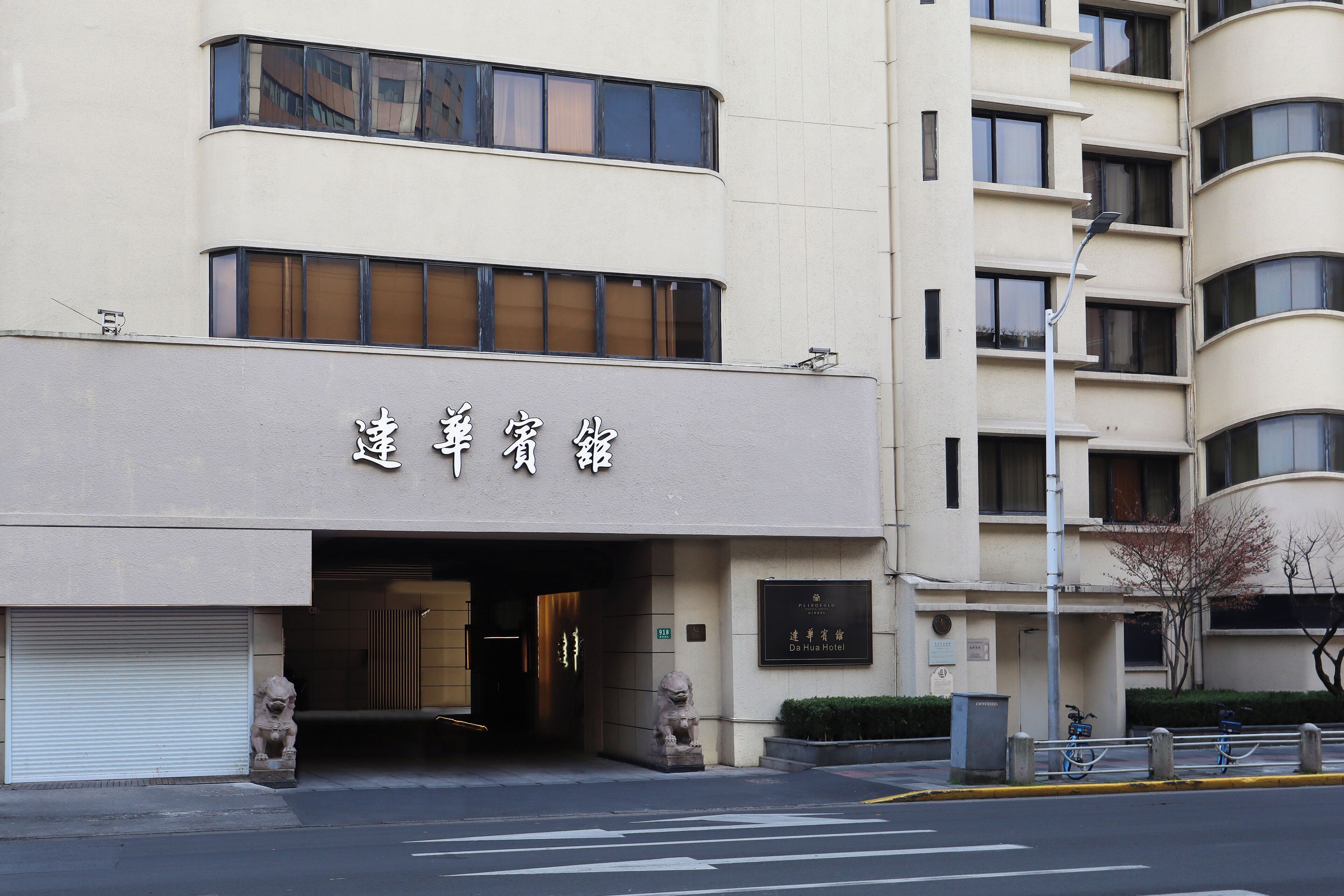 A hotel entrance with a sign in a foreign script, a statue, and a bike rack outside.
