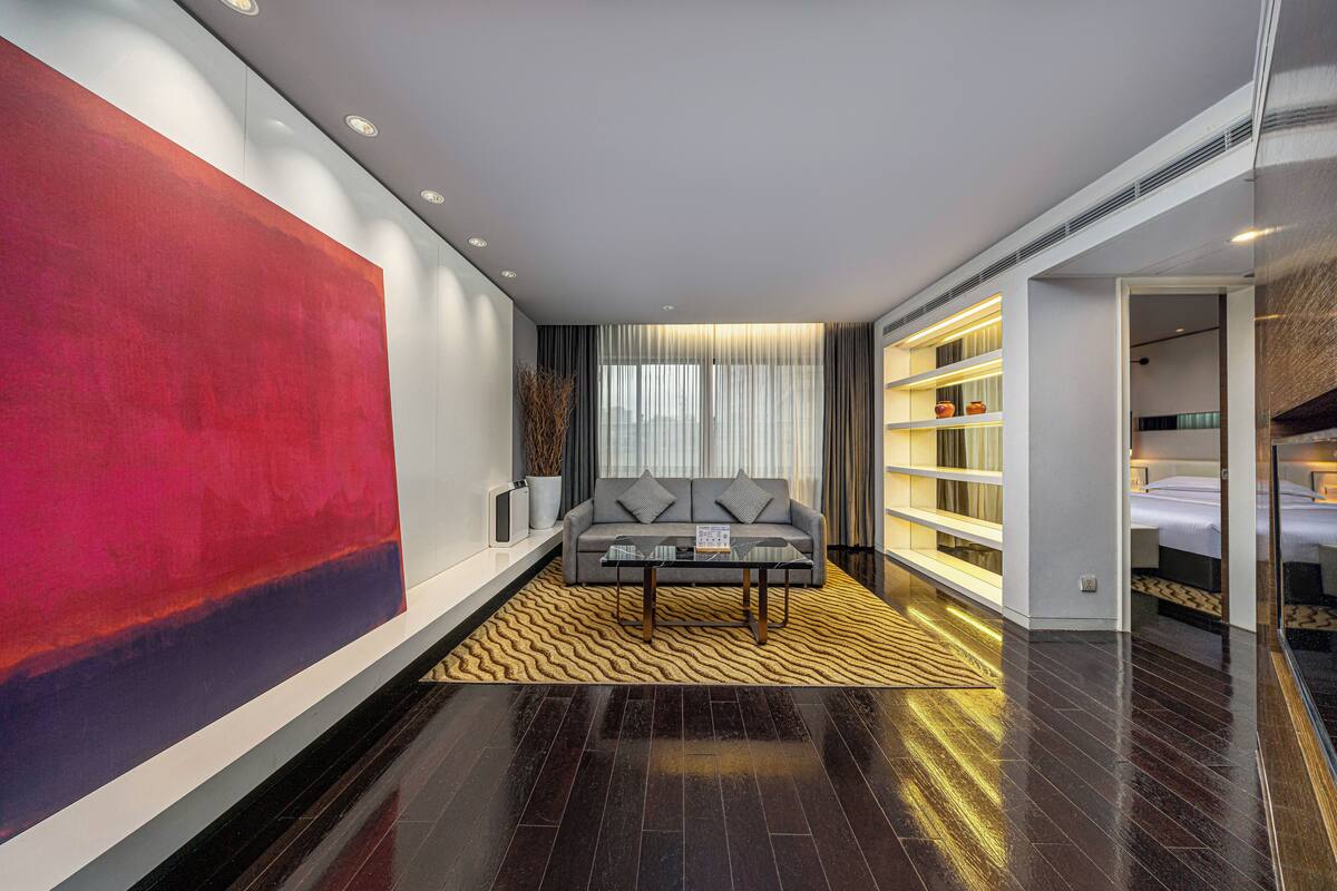 Una habitación de hotel moderna con un cuadro abstracto grande, un sofá, una mesita de centro y una estantería.