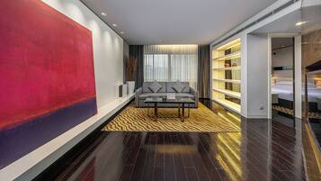 A modern hotel room with a large abstract painting, a sofa, a coffee table, and a bookshelf.