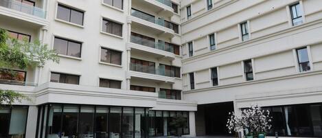 Un immeuble à plusieurs étages doté de balcons, d’un élément décoratif aquatique réfléchissant et d’un petit jardin agrémenté de fleurs.