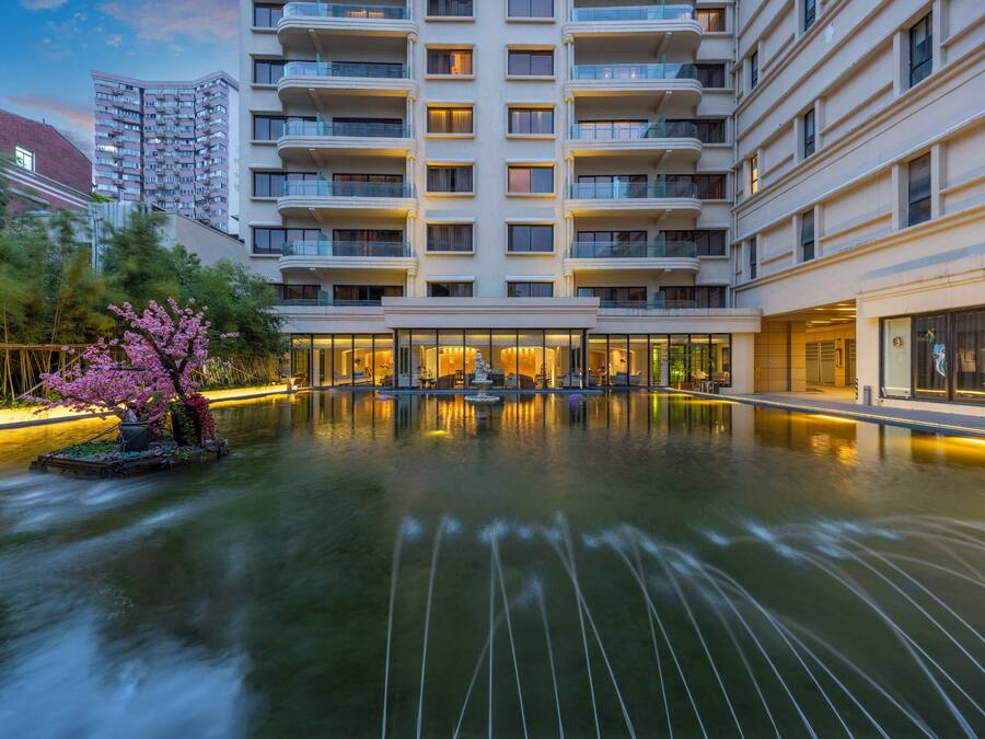 A modern hotel with a large indoor pool, surrounded by balconies and a well-lit entrance.