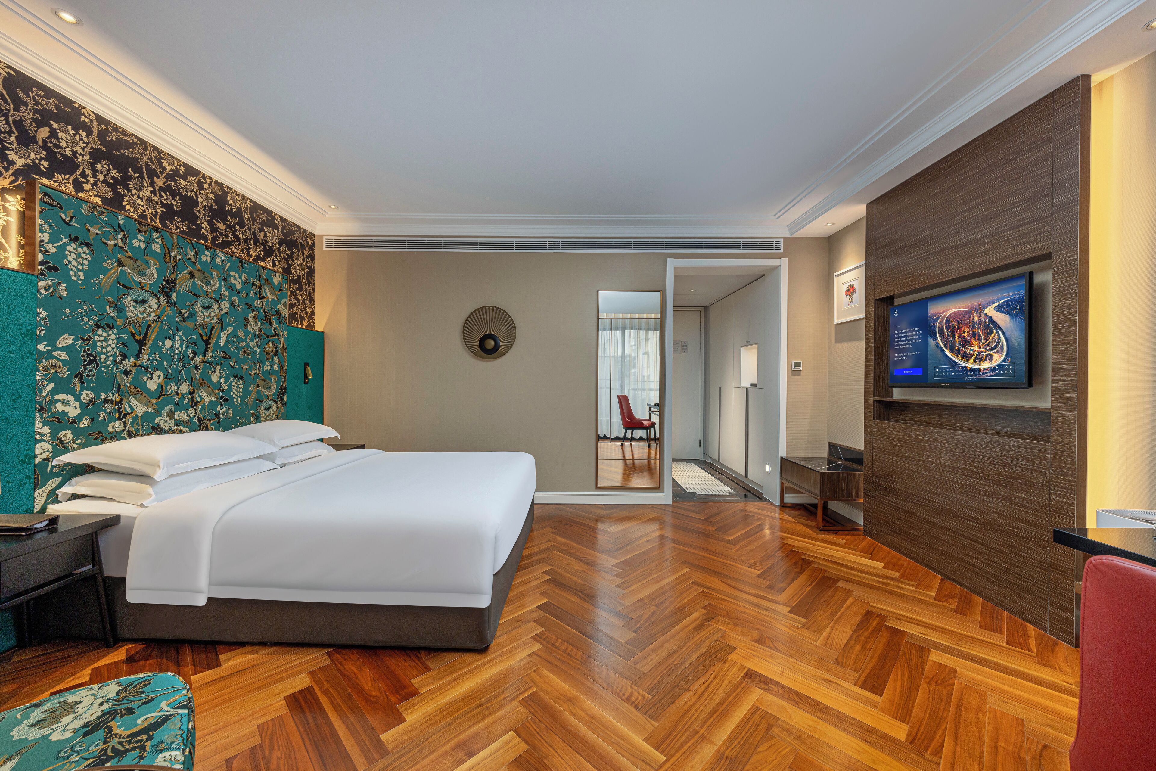 Una habitación de hotel moderna con una cama grande, un televisor montado en la pared y un suelo de madera con patrón de espiga.