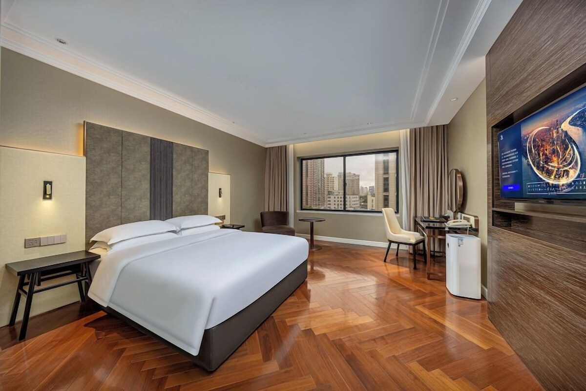 Una habitación de hotel con una cama grande, un escritorio, una silla, un televisor y vistas a la ciudad.