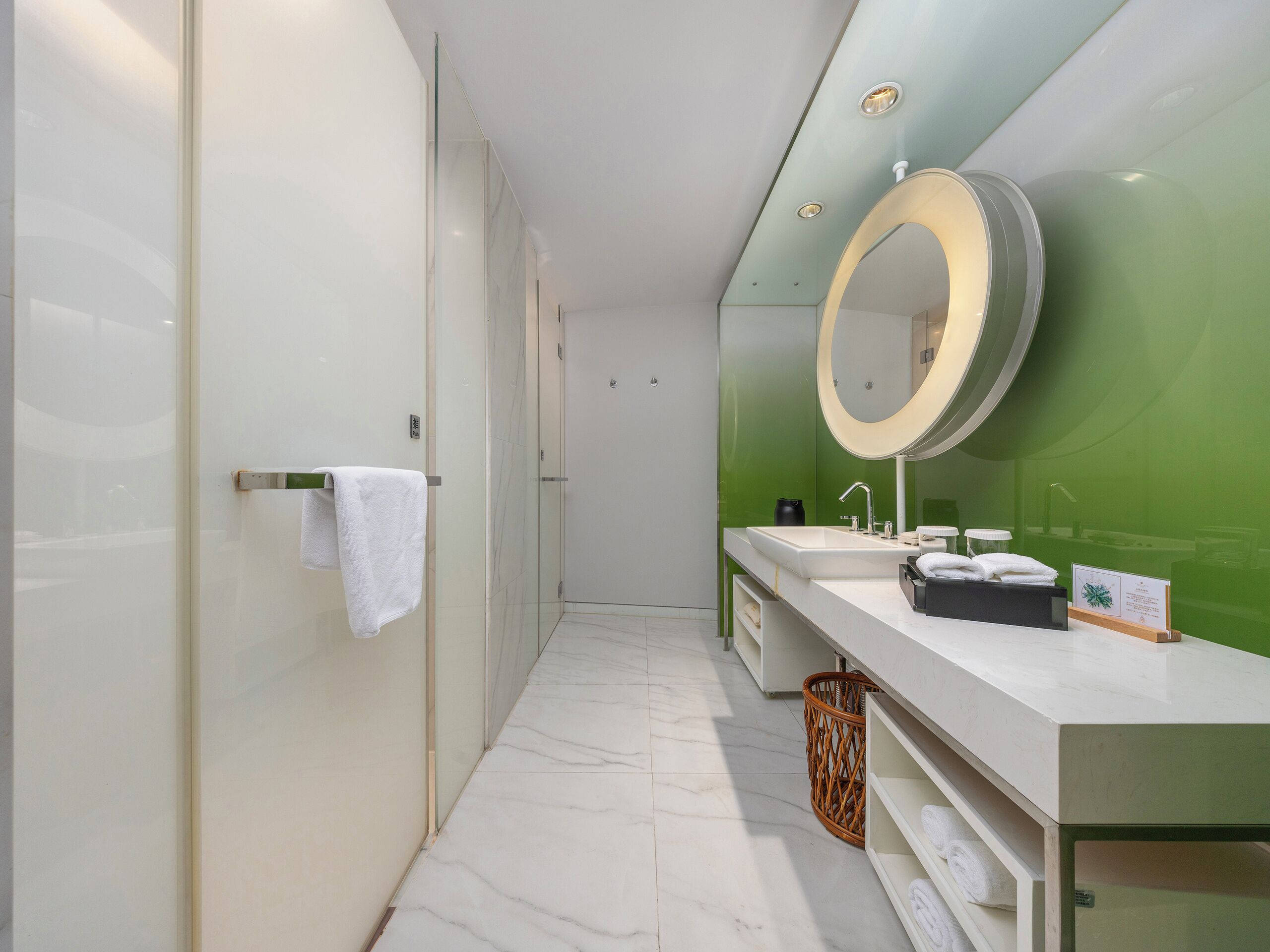 A modern bathroom with a glass shower enclosure, a white sink with a large mirror, and green walls.