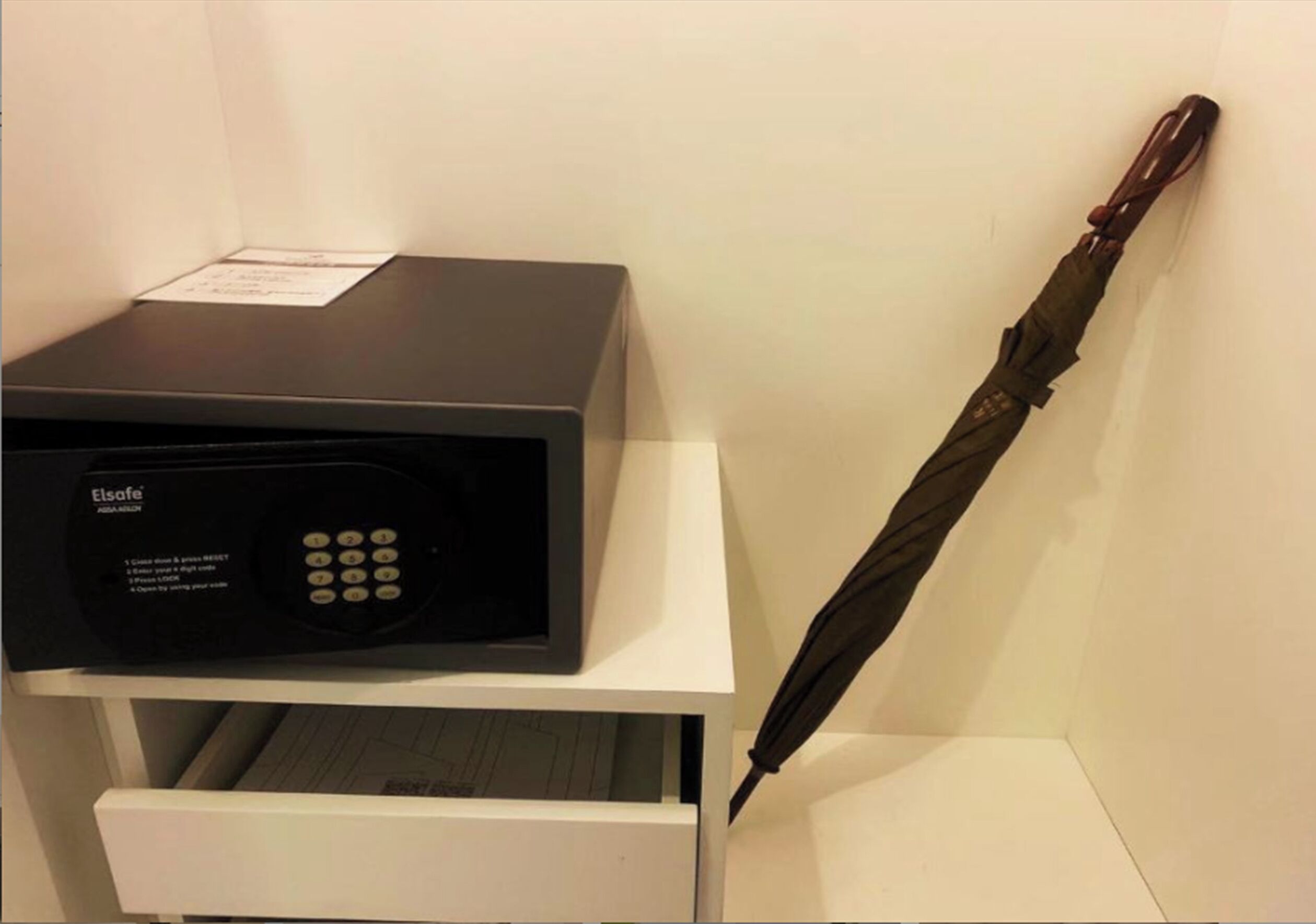 A black Elsanor safe on a white cabinet with a black umbrella leaning against the wall.