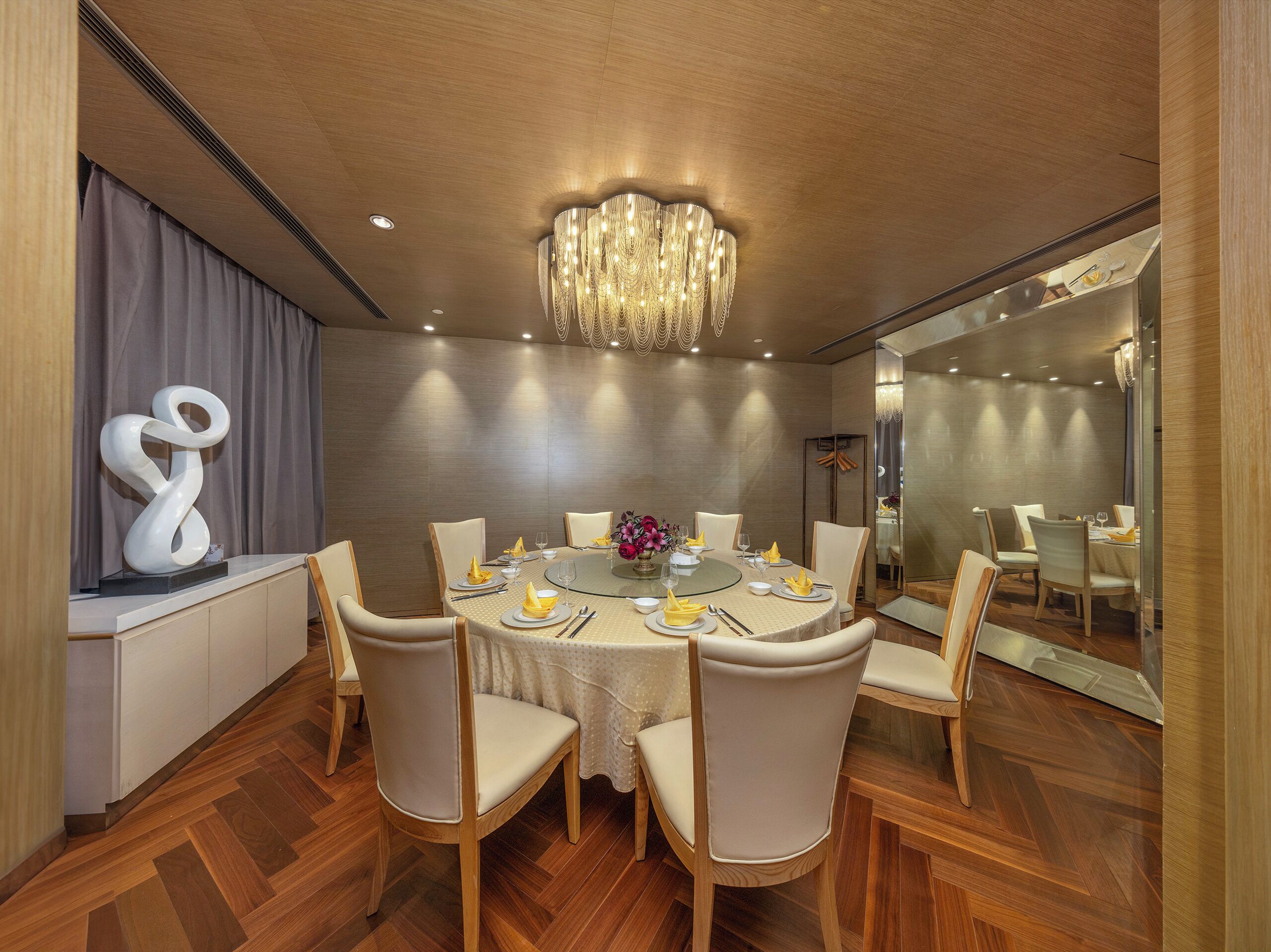 A modern dining room with a round table, white chairs, and a chandelier.