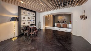 A modern lobby with a dark wood floor, a round table with stools, a black lamp, and framed pictures on the wall. - Metropolo Dahua Hotel Shanghai (Shanghai)