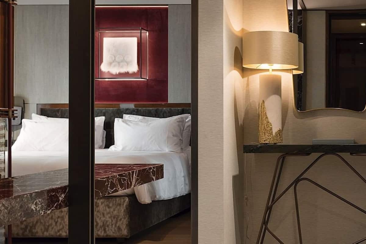 A hotel room with a bed, a marble bedside table, a wall-mounted lamp, and a mirror.