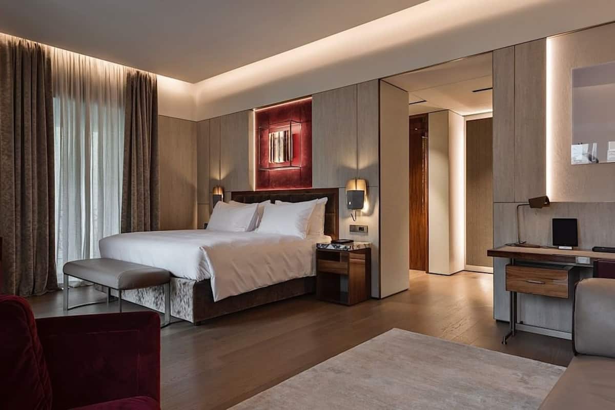 A modern hotel room with a large bed, a desk, a chair, and a large mirror.