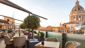 A rooftop terrace with wicker furniture, a small table, and a potted tree. - Fendi Private Suites (Rome)