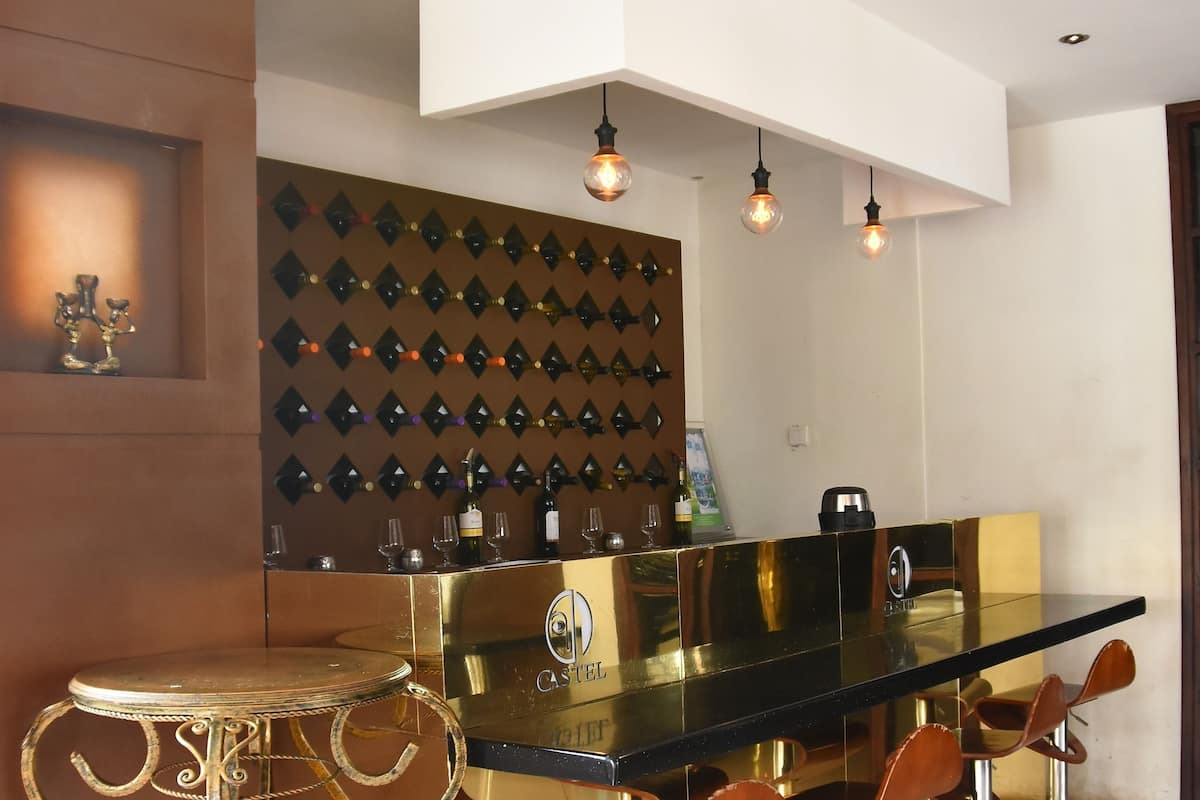 A modern bar area with a glass countertop, metal stools, and a decorative wall with wine glasses.