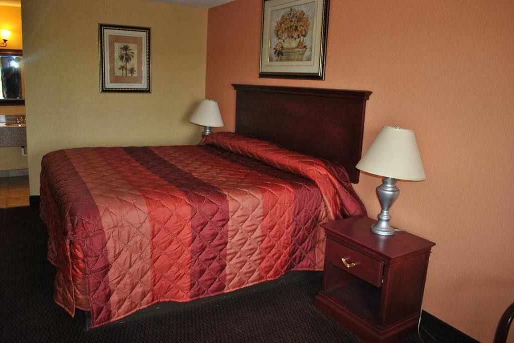Ein Hotelzimmer mit einem großen Bett, zwei Nachttischlampen, einem Nachttisch und zwei gerahmten Bildern an der Wand.