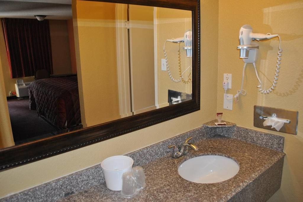 A hotel bathroom with a granite countertop, a sink, a mirror, and a hairdryer mounted on the wall.