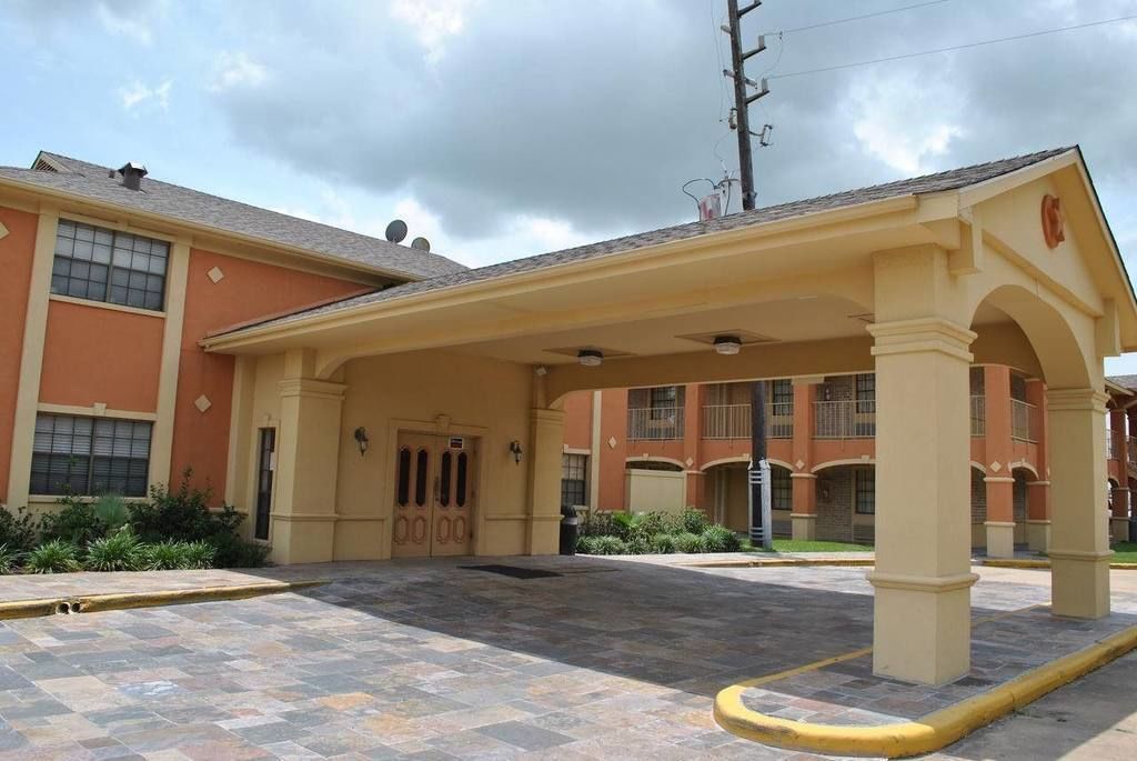 A hotel entrance with a covered walkway, a parking area, and a building with multiple windows and balconies.