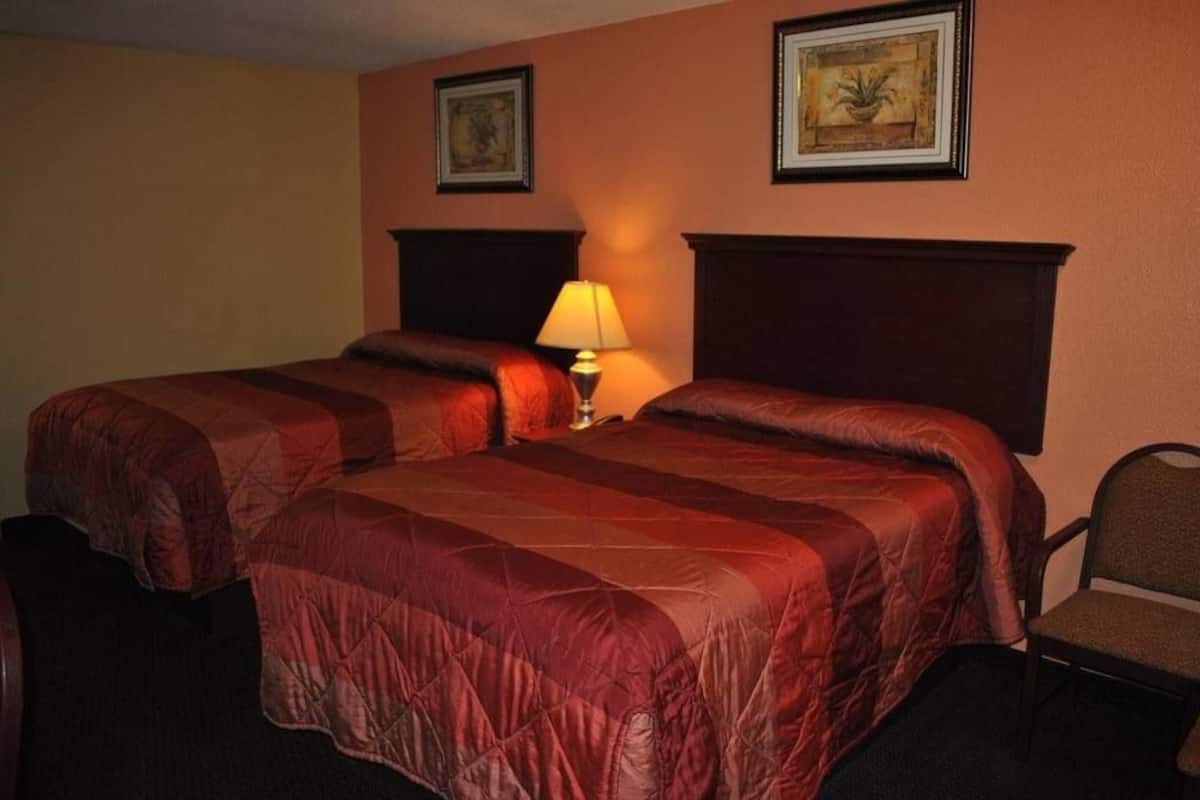 Quarto de hotel com duas camas, uma mesa de cabeceira com abajur e duas imagens emolduradas na parede.