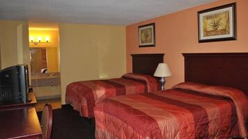 Habitación de hotel con dos camas, un escritorio, un televisor y un baño con espejo e iluminación.