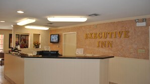 Zona de recepción con pared de mármol, mostrador de recepción y televisor montado en la pared.