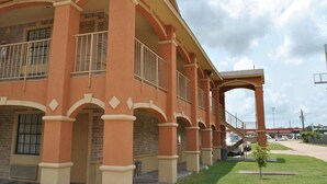 Un edificio con una serie de arcos y columnas, un corredor cubierto y un pequeño árbol en primer plano.