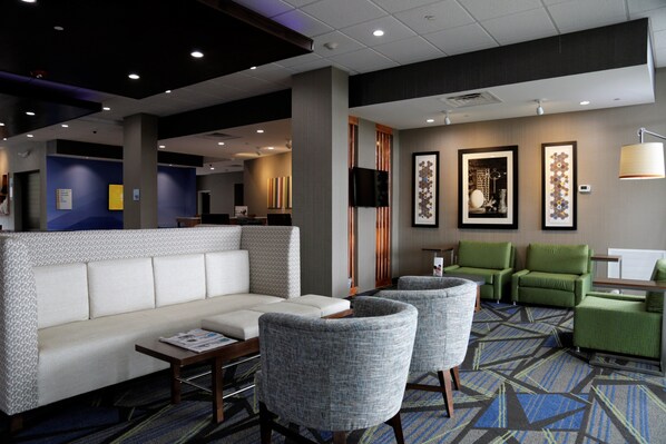 Un hall de hotel con un sofá, sillones, una mesita, un televisor y obras de arte enmarcadas en las paredes.