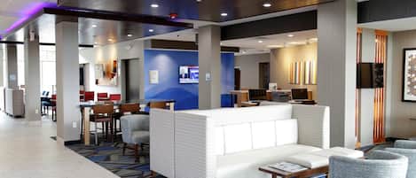 A hotel lobby with a seating area, a reception desk, and a television screen.
