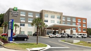 A Holiday Inn Express & Suites building with a modern design, featuring a mix of stone and glass facade, a parking lot with several cars, and a flagpole with the American flag. - Holiday Inn Express & Suites Alabaster by IHG (Alabaster)