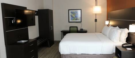 A hotel room with a large bed, a desk with a computer, a TV, and a bedside lamp.